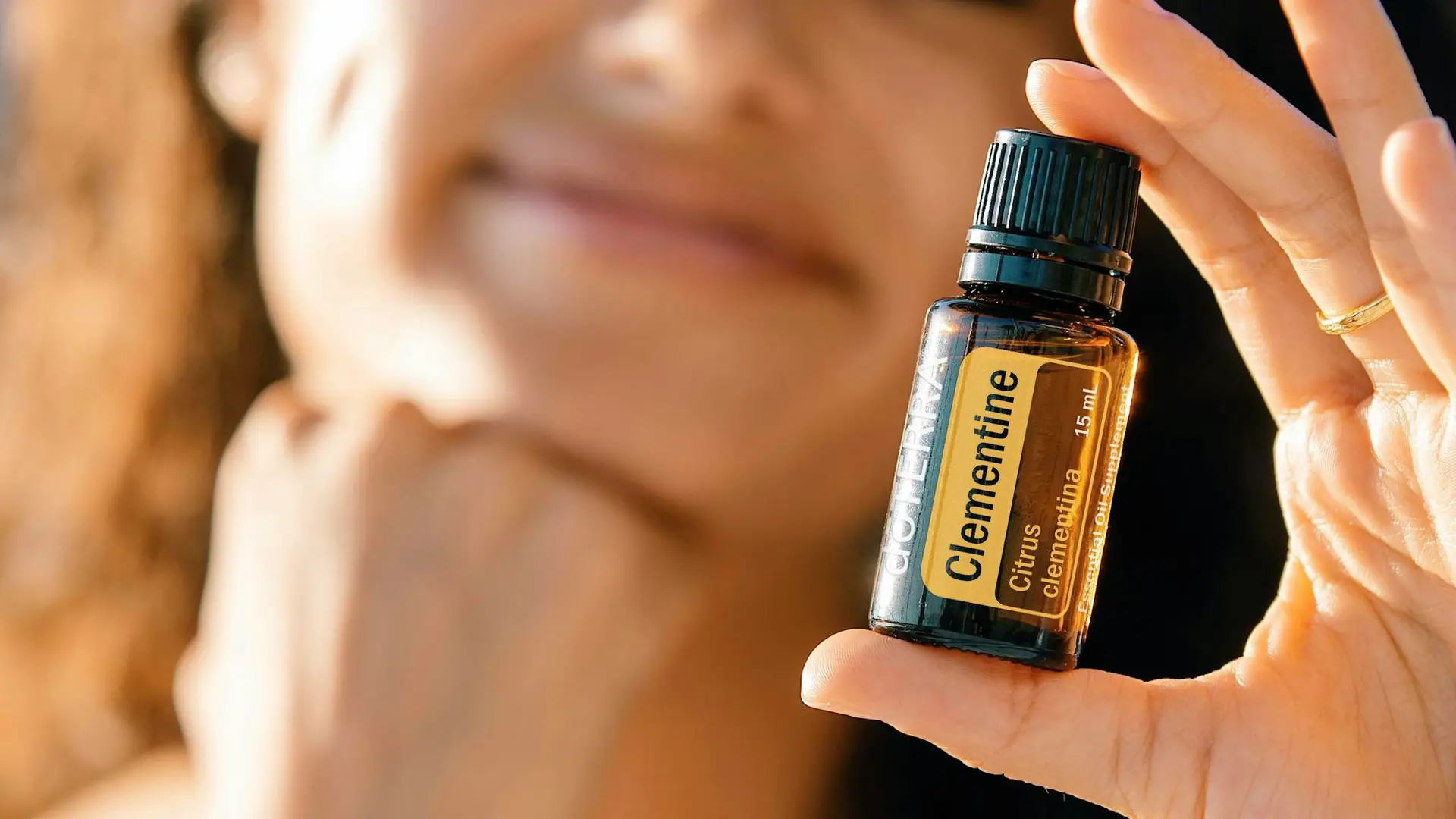 A close-up image of a woman holding a Clementine essential oil bottle, highlighting natural skincare.