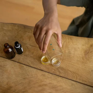 A person making natural lip balm with essential oils on a wooden table.