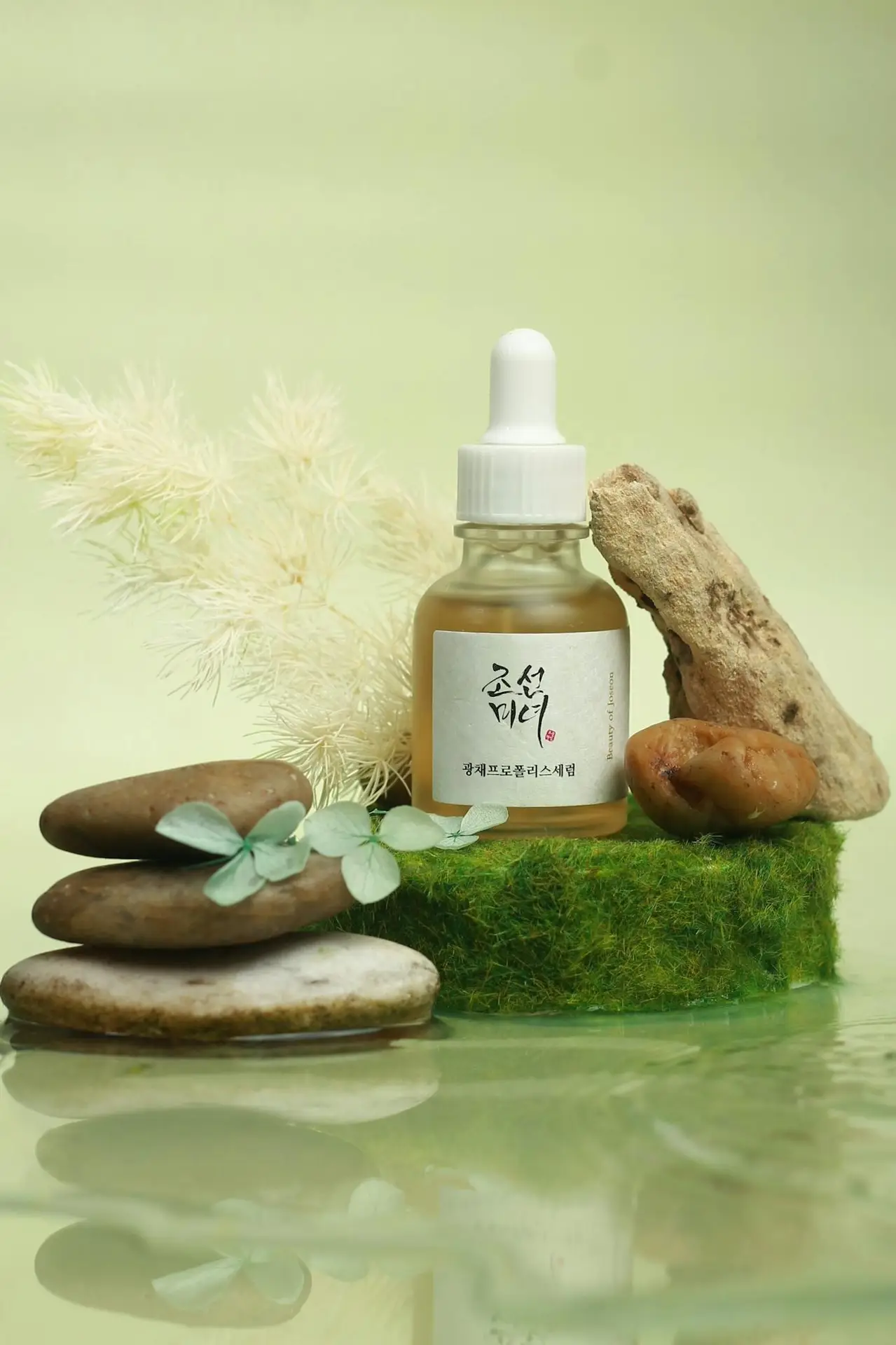 Serum bottle with natural elements and stones on a green background.